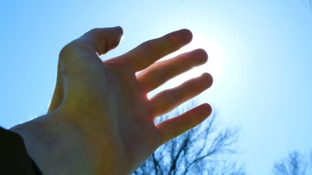 Mão do homem dedos brinca com os raios sóis contra o céu azul — Vídeo de Stock