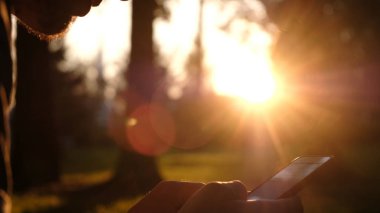 Adam bir akıllı telefon kullanan ve gün batımı yakın çekim parkta, kamera hareketi, ekranda bir ileti yazdırır