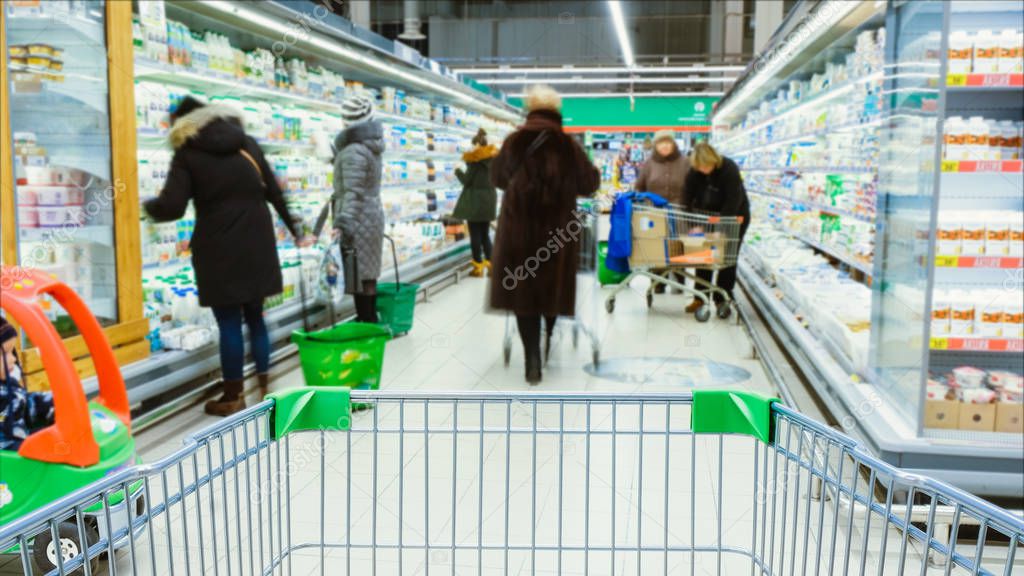 Timelapse - shopping trolley stands on the background of blurred customers in the aisle, people choose products