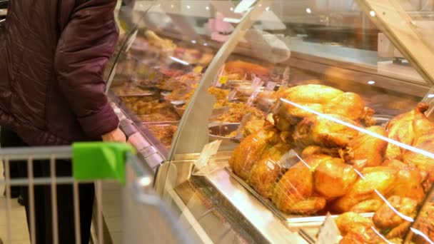 Une femme âgée choisit un poulet frit sur l'écran dans un supermarché. Les gens achètent des aliments. Industrie alimentaire au détail . — Video