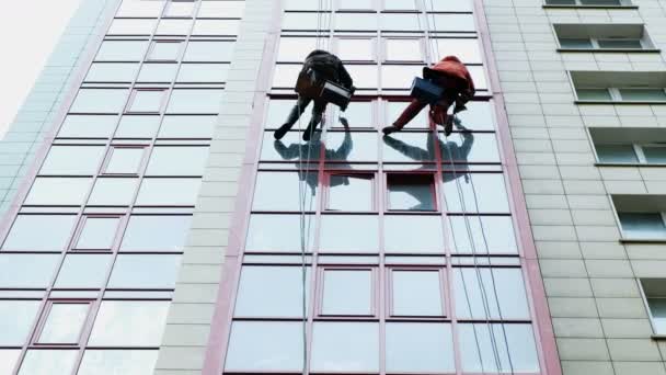 Twee industriële klimmers zijn wassen, reinigen van de gevel van een modern kantoorgebouw — Stockvideo