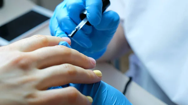 Nail master applies firming nail polish on nails in beauty salon, close-up