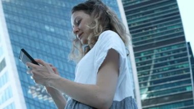 Genç güzel kız bir smartphone gökdelenler arka plan üzerinde kullanır.