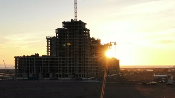 Fotografering från en drone under konstruktion bostadshus med byggkranar i solnedgången, flyger drone upp till byggarbetsplatsen — Stockvideo