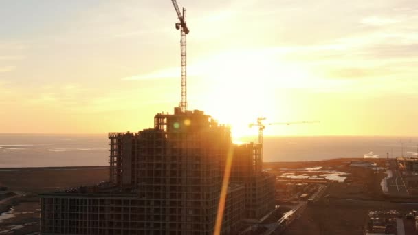 Vliegen over de bouwplaats, het werk van de bouw kranen en werknemers bij zonsondergang, aerial view — Stockvideo