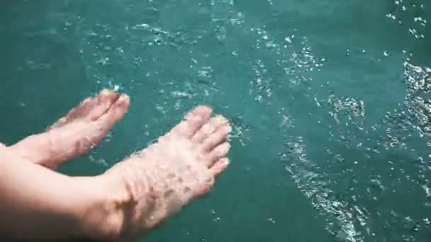 Vergődő érzik magukat a parton, a lány lába világos türkizkék vízben a lassú mozgás — Stock videók