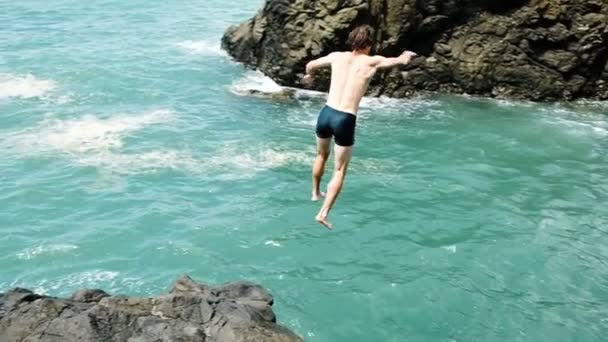 O homem salta de um penhasco para o mar em câmara lenta. Divertir-se nas férias de verão . — Vídeo de Stock