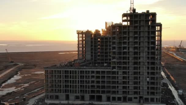 Vol de la construction d'un bâtiment de plusieurs étages sur le fond des rayons du coucher du soleil sur le bord de la mer — Video