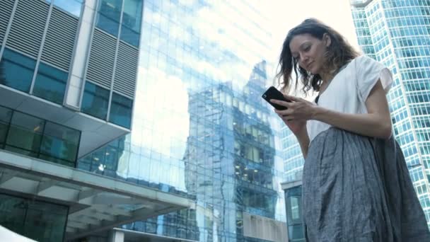Frau benutzt Smartphone vor dem Hintergrund von Geschäftszentren auf der Straße — Stockvideo