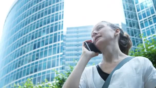 Zakelijke vrouw praten over de telefoon en gebaren met de hand op de achtergrond van wolkenkrabbers — Stockvideo