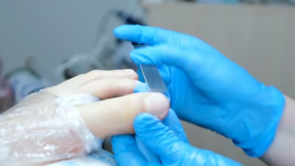 Pédicure maître scie la plaque à ongles sur les jambes fermer, les pieds sont enveloppés dans une pellicule plastique — Video