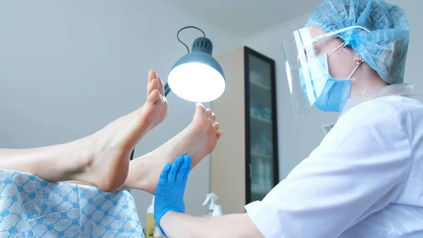 Дівчина-педикюр з захисною маскою наносить крем на ноги і робить масаж клієнту — стокове фото
