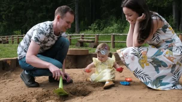 Familia feliz con un niño jugando en la caja de arena - padre construye estatuillas de arena para su hija — Vídeos de Stock