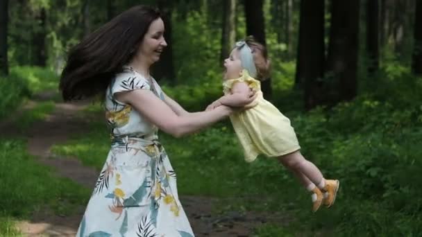 Madre está dando vueltas con la niña en sus brazos, riendo y sonriendo en el bosque, cámara lenta — Vídeos de Stock