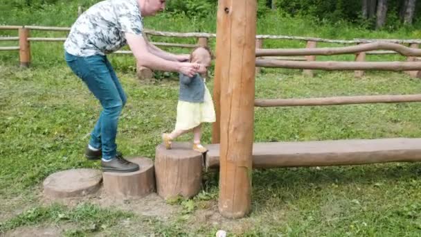 Handsome man helps toddler daughter walk along park log — Stock Video