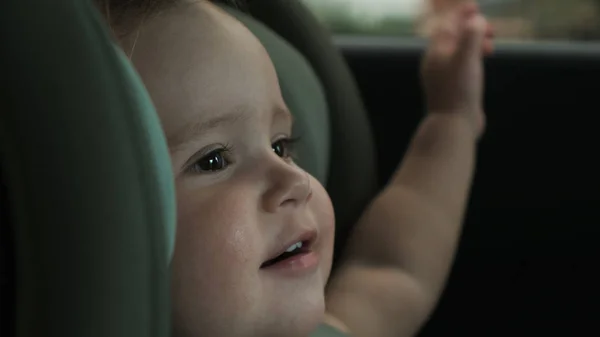 Criança senta-se no assento de segurança do carro da criança e olha para fora da janela — Fotografia de Stock
