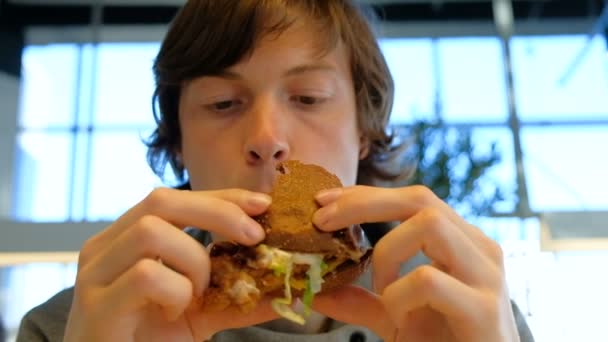 Concentrado chico sostiene hamburguesa y mastica primer plano — Vídeo de stock