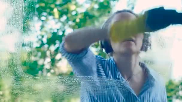Meisje veegt vuile venster met blauwe Rag luisteren naar muziek — Stockvideo
