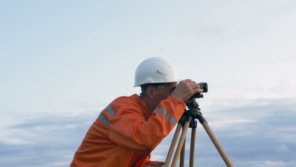 Zkušený inspektor v oranžovém kombinézu a přilbě na teodolitu — Stock video