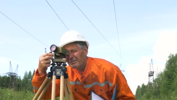 Пожилой геодезист смотрит через тупой уровень бинокля и отмечает — стоковое видео