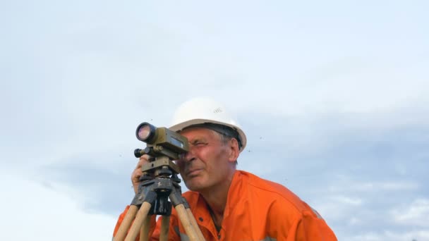 Surveyor looks through level under blue sky with clouds — Stock Video