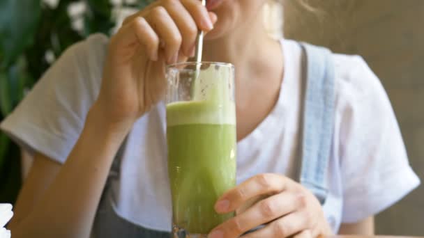 Mujer joven bebe bebida fresca verde en la mesa de madera — Vídeo de stock