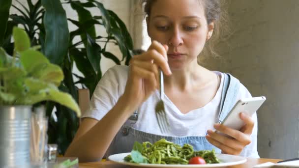 Morena hermosa tipos en el teléfono inteligente y come ensalada fresca — Vídeos de Stock
