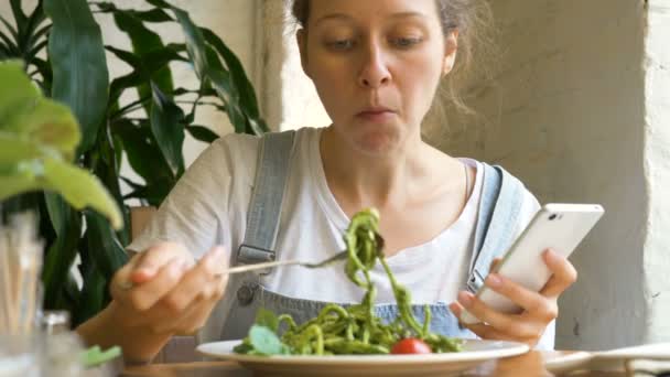 Brunette student eats green fresh salad holding smartphone — Stock Video