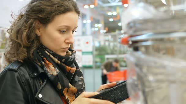 Кудрявая девушка внимательно читает инструкции на сковороде в гипермаркете — стоковое видео