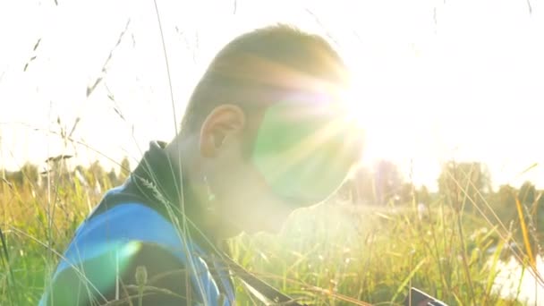 Little Boy neemt Foto's met een digitale camera en opent het vouwscherm van de camera in het gras bij zonsondergang — Stockvideo