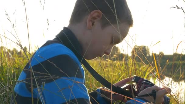 Маленький хлопчик фотографує на цифровій камері і дивиться на поворотний екран на заході сонця — стокове відео