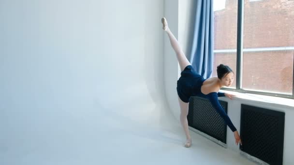 Balletttänzer im blauen Kleid streckt sich am Fenster stehend — Stockvideo