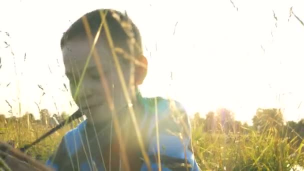 Хлопчик лежить на зеленому полі трава тримає ретро камеру в руках — стокове відео