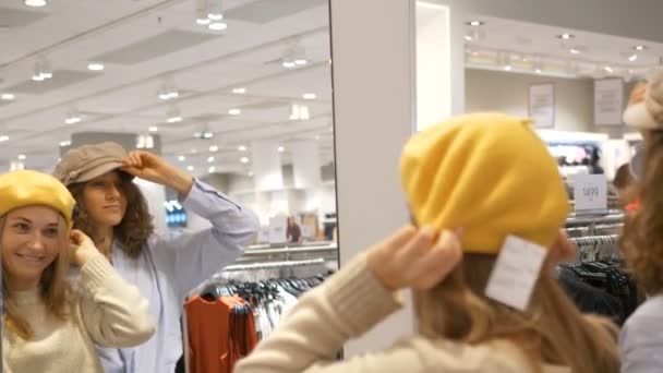 Lány barátok töltenek hétvégén a boltban kiválasztás kalap és tánc — Stock videók
