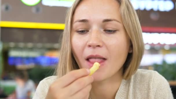 Vrouw eet frietjes en glimlacht zittend in winkelcentrum cafe — Stockvideo