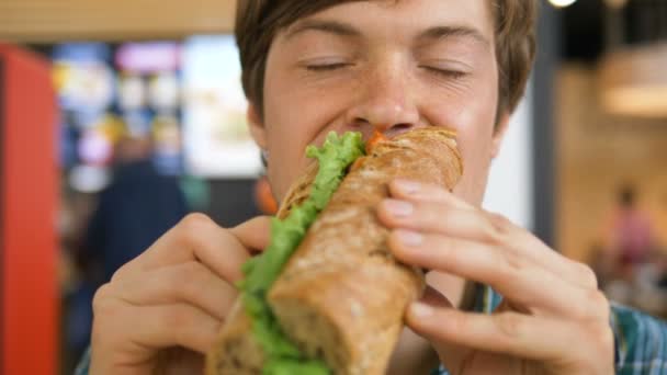 Guy eats hot dog and enjoys lunch sitting in shopping mall — Stock Video