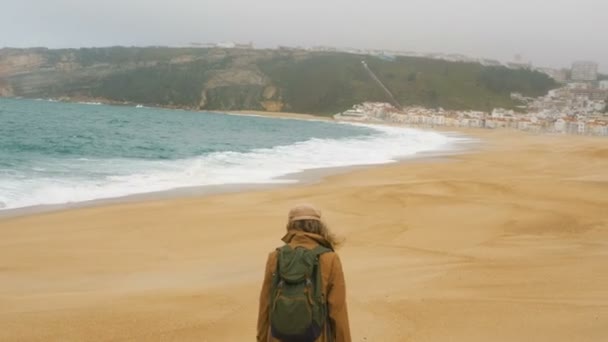 Girl tourist walks along golden sand beach against city — Stock Video