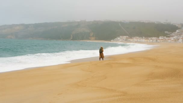 Frau läuft am Strand entlang, angespült von stürmischem Meer gegen Hügel — Stockvideo