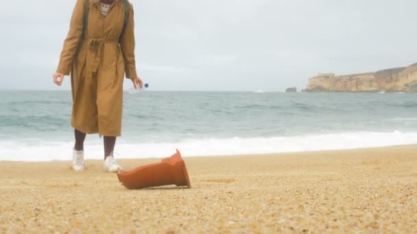 Женщина-турист собирает выброшенные человеческие отходы на берегу океана — стоковое видео
