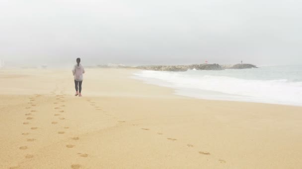 Спортивна жінка біжить на золотому пляжі залишаючи сліди піску — стокове відео