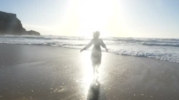 Woman runs on sand beach towards bright sun rays above ocean — Stock Video