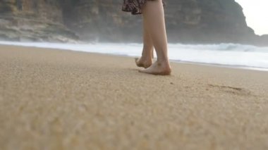 Kadın bacakları altın plaj boyunca yürür arkasında ayak izleri bırakır.