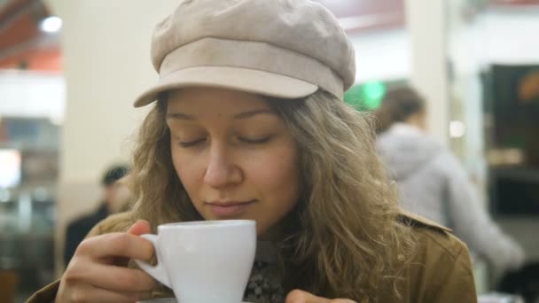 Retrato de una hermosa chica bebiendo una taza de café en la terraza en un café de verano con una gorra de reportero — Vídeos de Stock