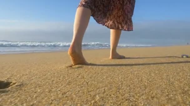 Menina em um vestido caminha ao longo do oceano descalço na areia closeup, uma onda lava os pés com salpicos câmera lenta — Vídeo de Stock