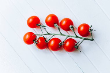 Beyaz ahşap arka planda yeşil bir dal üzerinde sulu olgun domatesler.