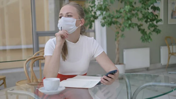 Vrouw met notebook en telefoon neemt af masker om koffie te drinken — Stockfoto