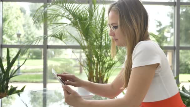 Blond zakenvrouw in bril surft internet met tablet — Stockvideo