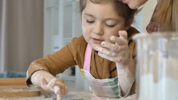 Mãe e filha fazem biscoitos de férias juntos na cozinha. Uma menina ajuda sua mãe, recolhendo a farinha no copo. — Vídeo de Stock