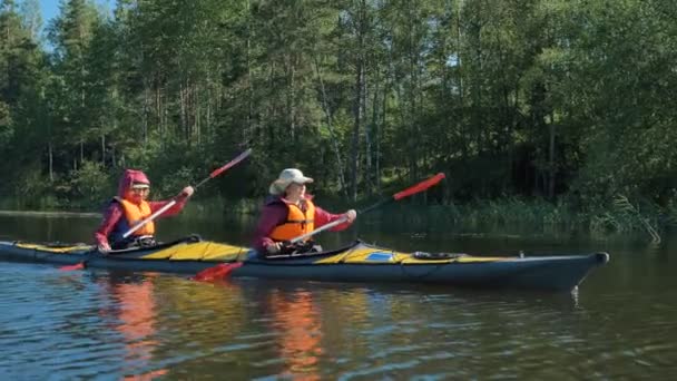 Lidé v vestách a čepicích plachty kajak podél klidné řeky — Stock video