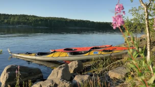 Kayalık göl kıyısında spor kanoları ve pembe çiçekler. — Stok video